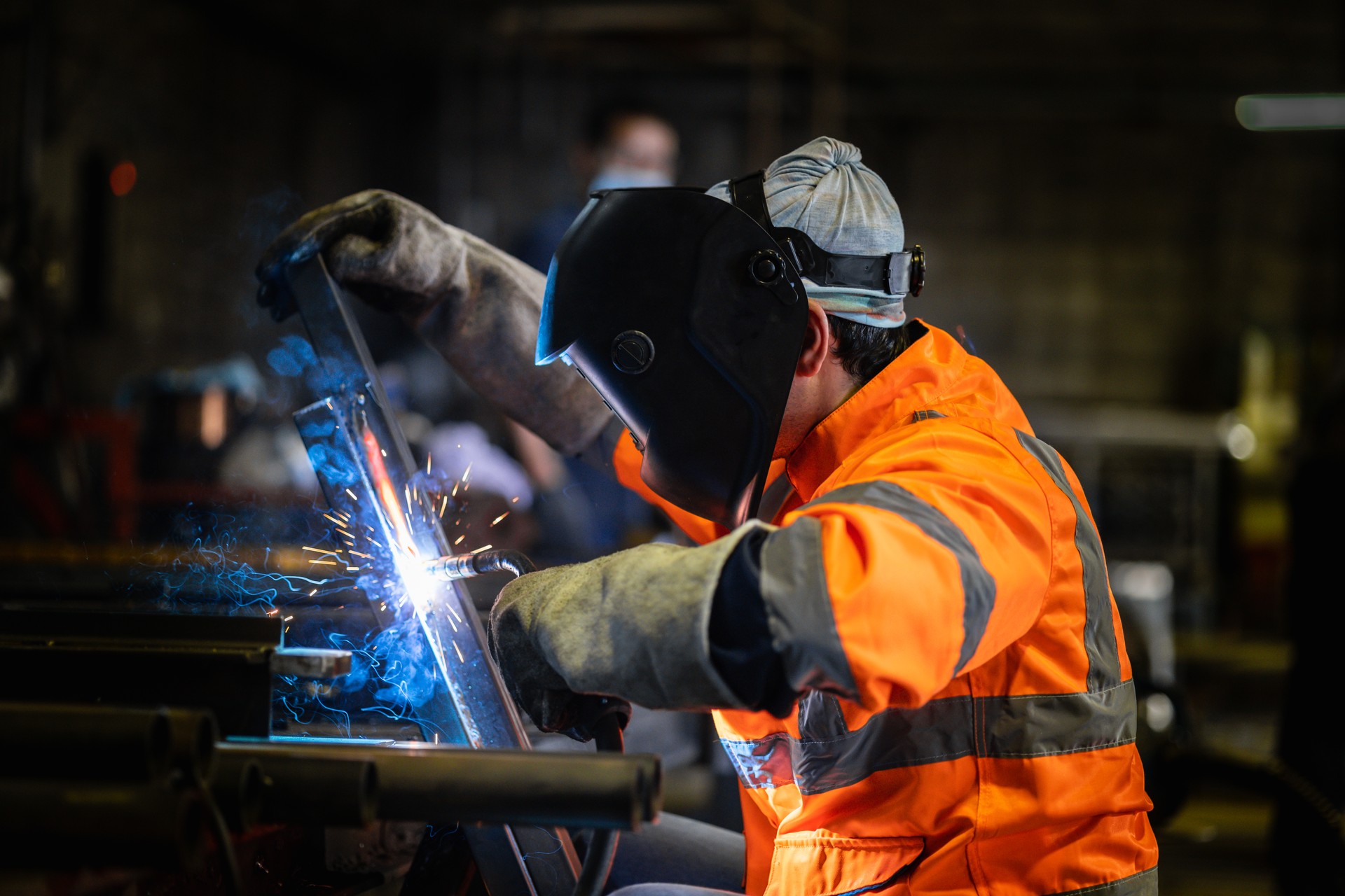 Closeup workers wearing industrial uniforms and using electric arc welding machine to weld steel at factory. Metalwork manufacturing and construction maintenance service by manual skill labor concept.